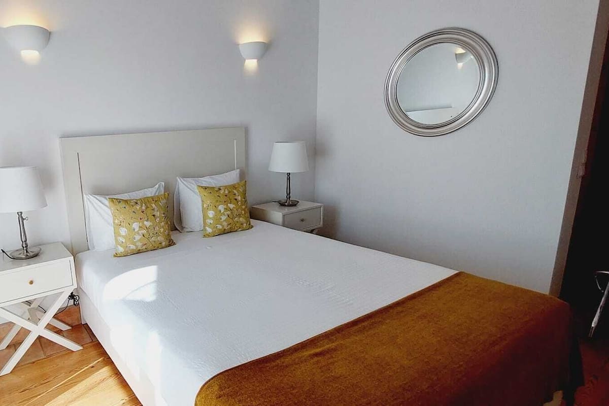 A bedroom with a bed, two bedside tables, a mirror, and a window with curtains.