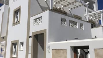Un edificio moderno con fachada blanca, varios balcones y grandes macetas con plantas.