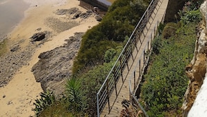 A coastal property with a beach, a small building with a red roof, and a rocky cliff.