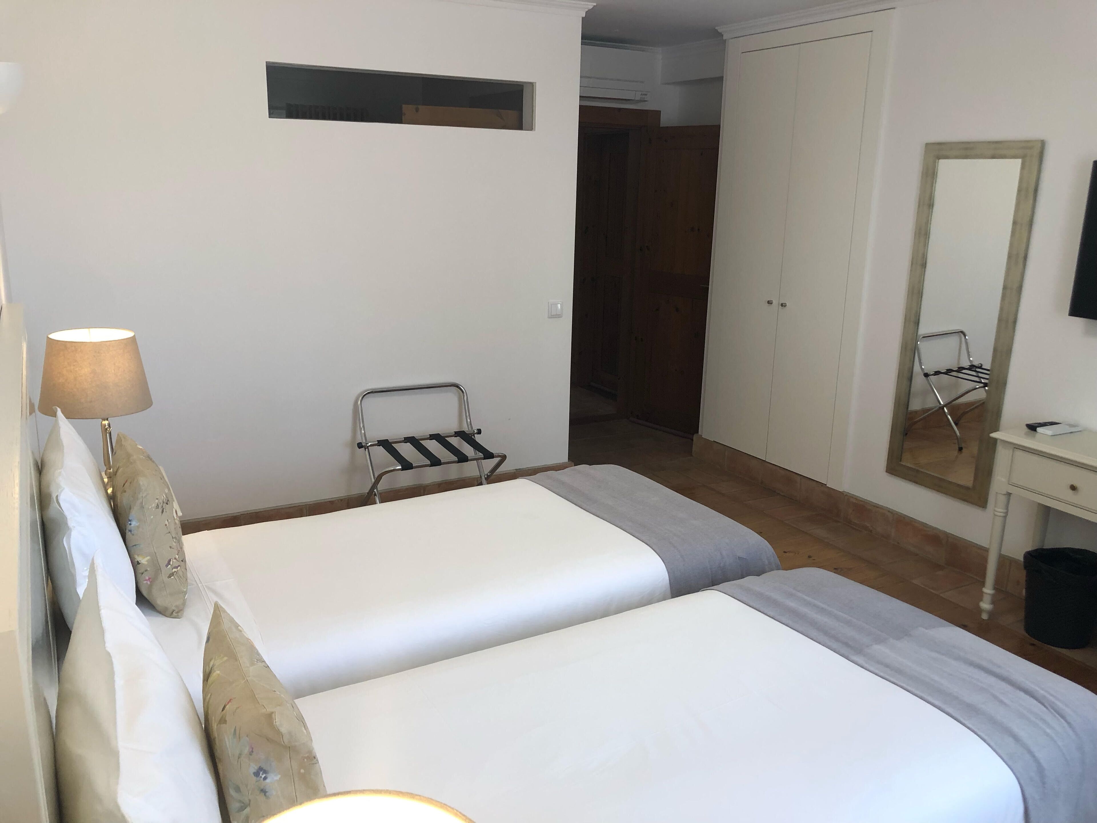 Une chambre d’hôtel avec deux lits, une table de chevet, une lampe, un miroir et une armoire.