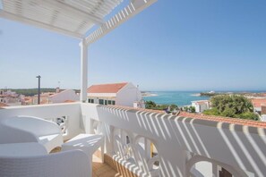A balcony with white furniture and a view of the sea and buildings.