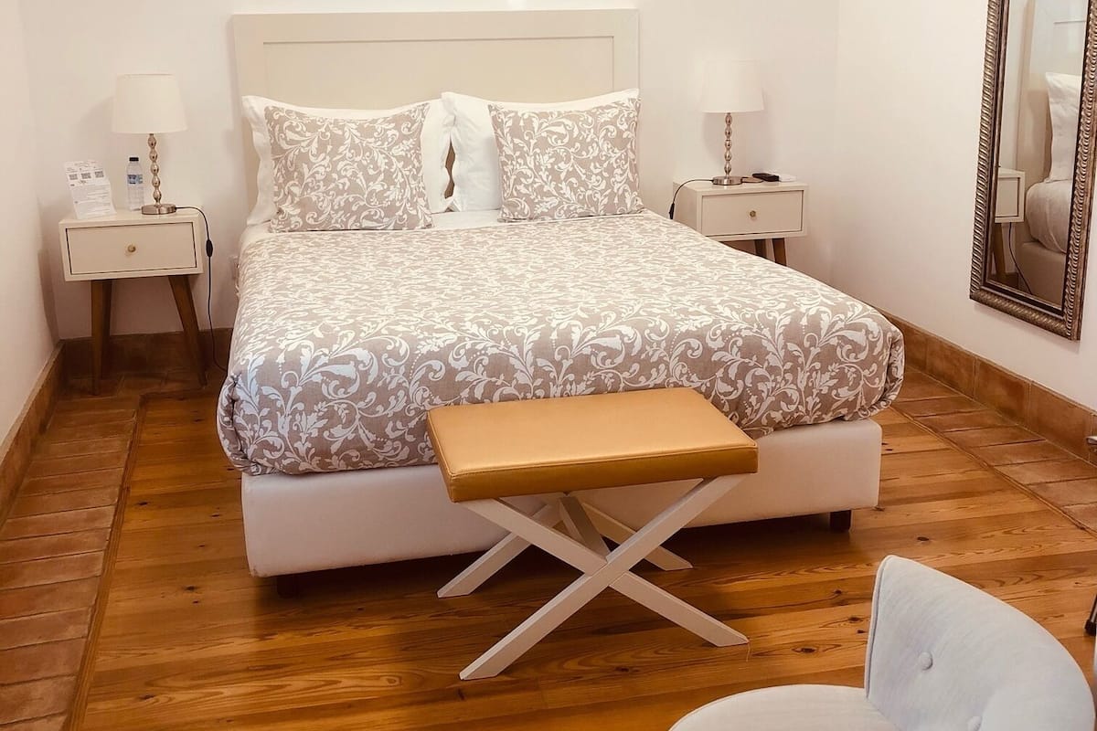 A bedroom with a bed, bedside tables, a bench, a chair, and a mirror.
