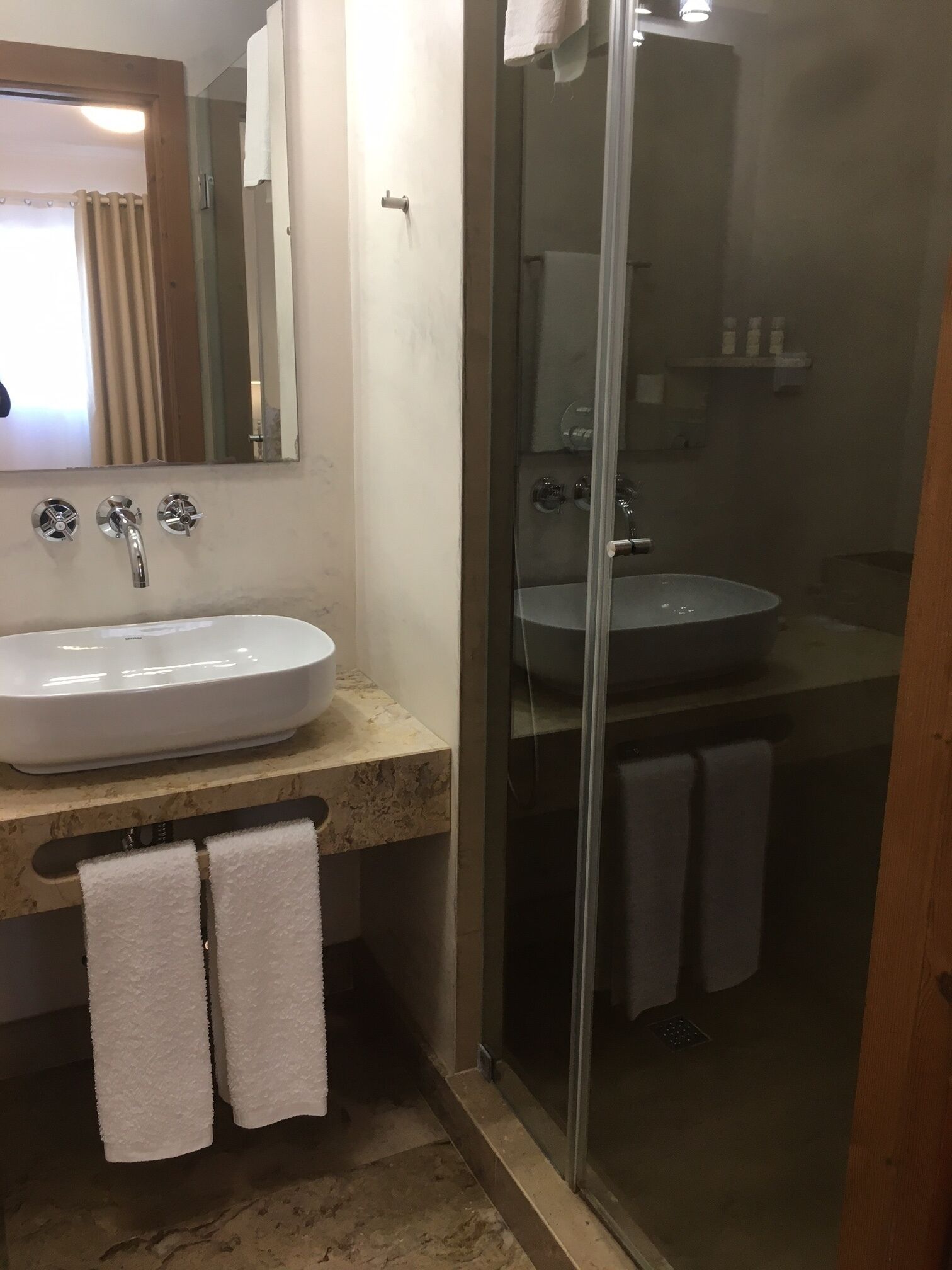 Un bany amb un lavabo blanc, un mirall i una zona de banyera amb portes de vidre.