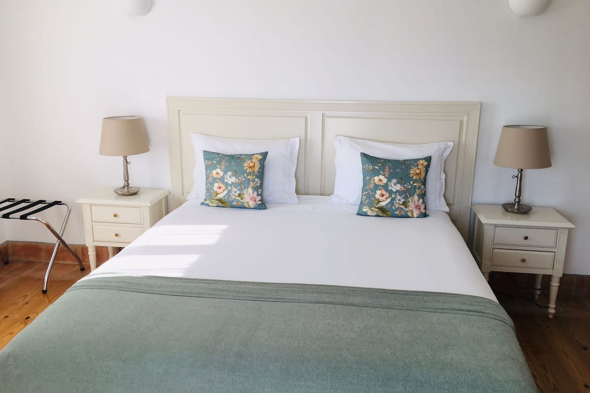 A neatly made bed with floral pillows, a bedside table with a lamp, and a nightstand with a lamp.