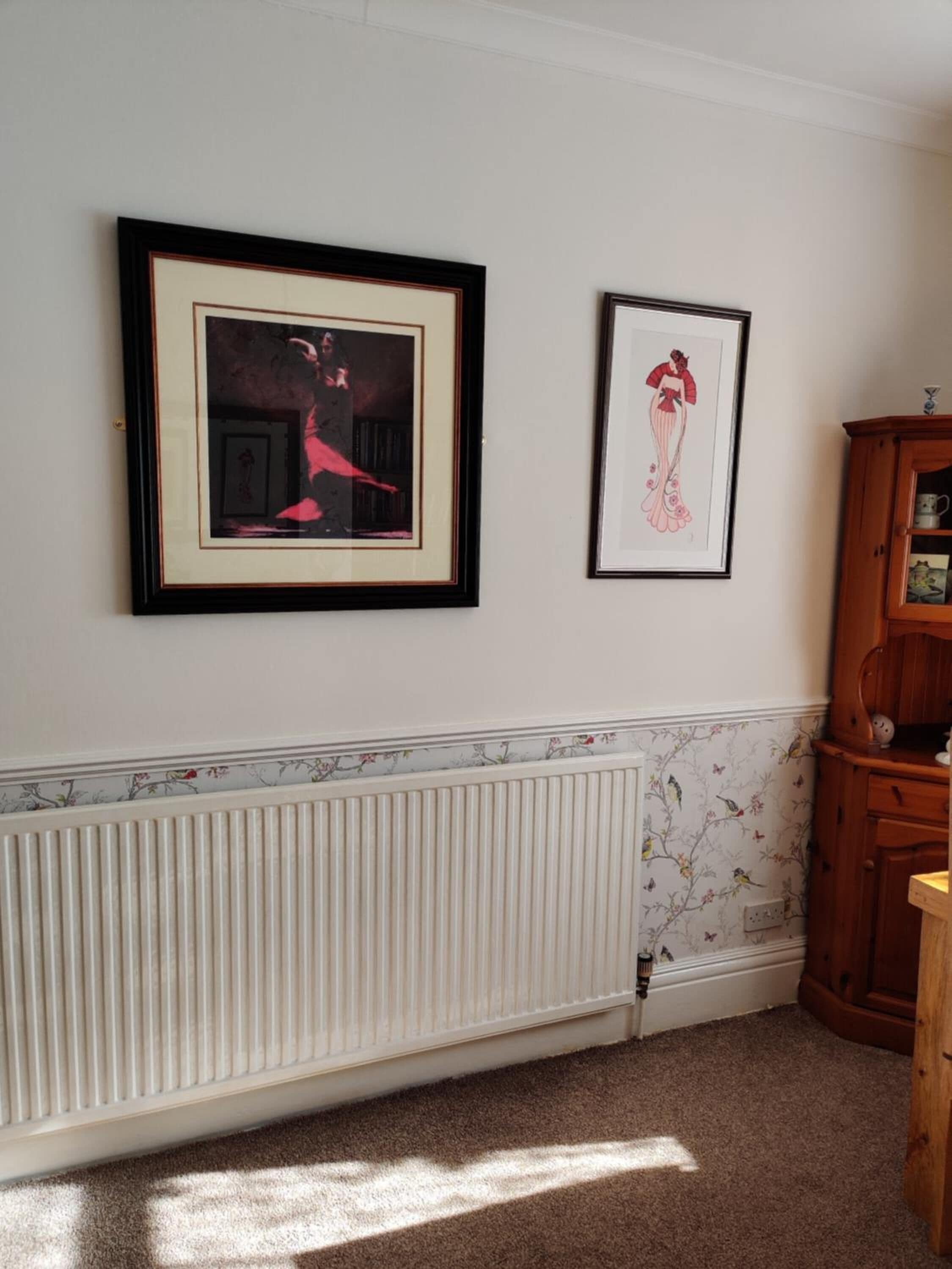 Una habitación con un radiador, un armario de madera y dos cuadros en la pared.
