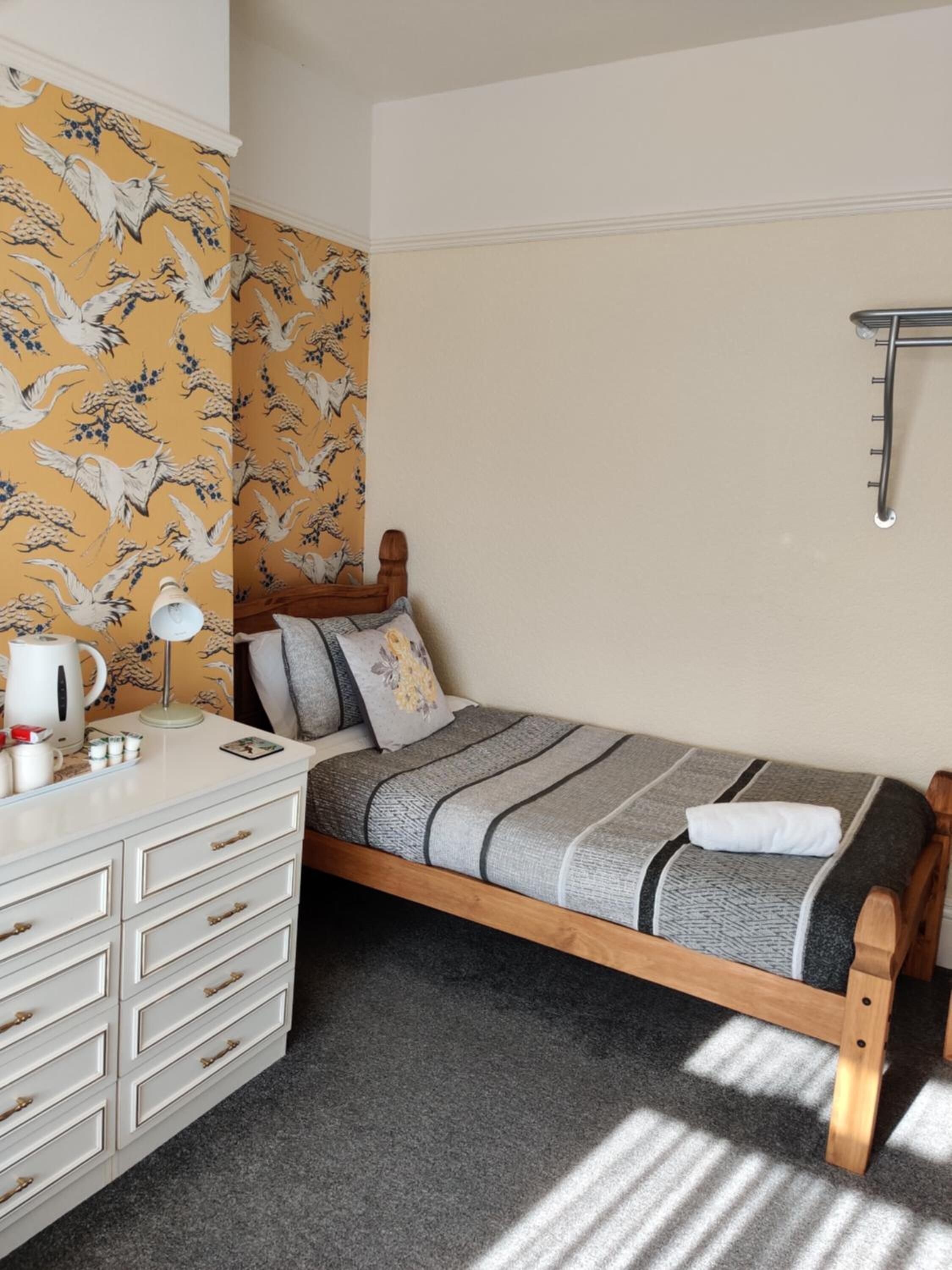 A small, neatly arranged bedroom with a bed, a dresser, and a wall-mounted shelf.