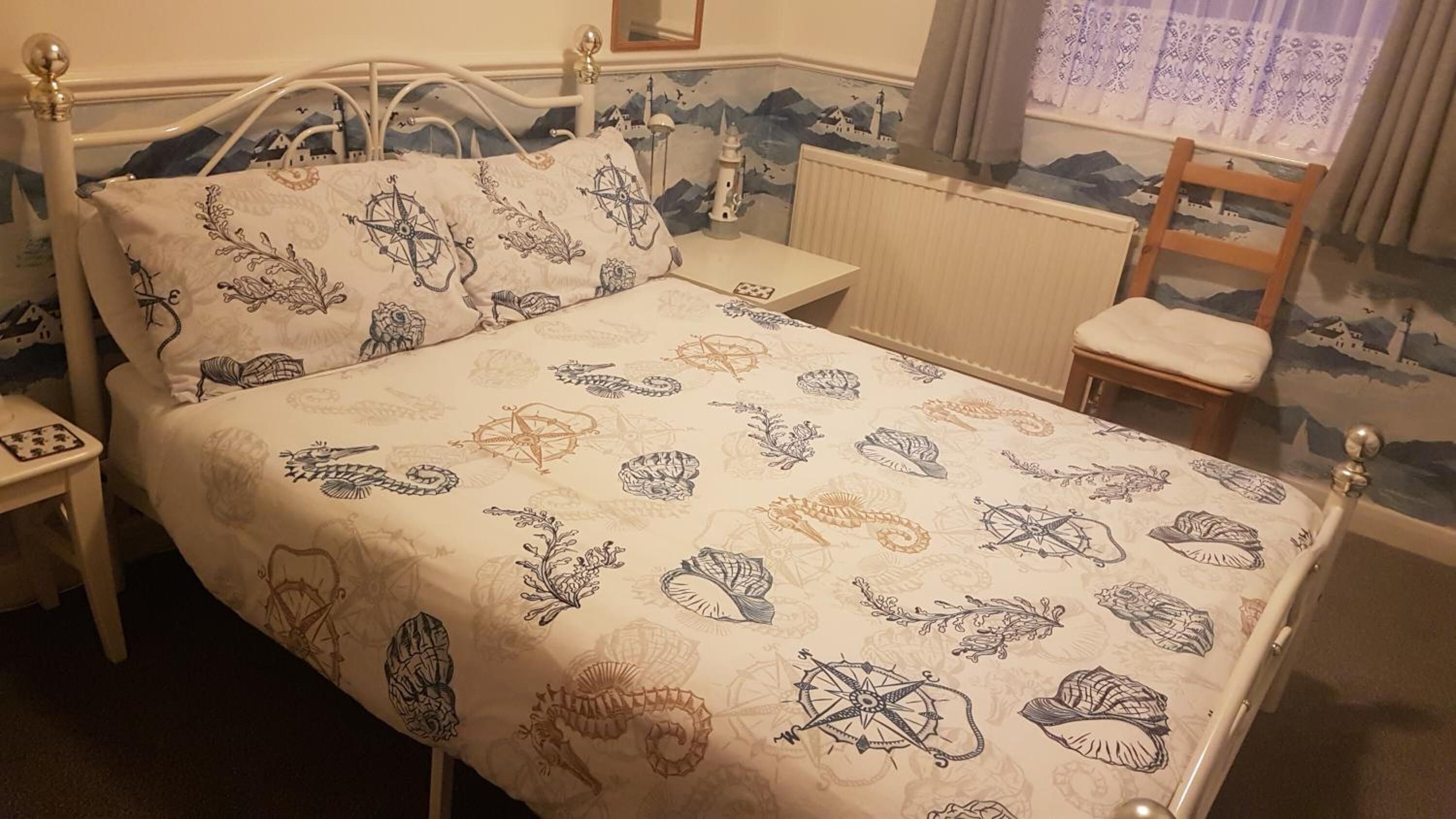 Ein Bett mit gemustertem Bettbezug, ein Nachttisch, ein Sessel und ein Beistelltisch.