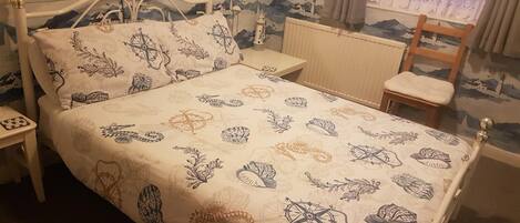 A bed with a patterned bedspread, a bedside table, a chair, and a nightstand.
