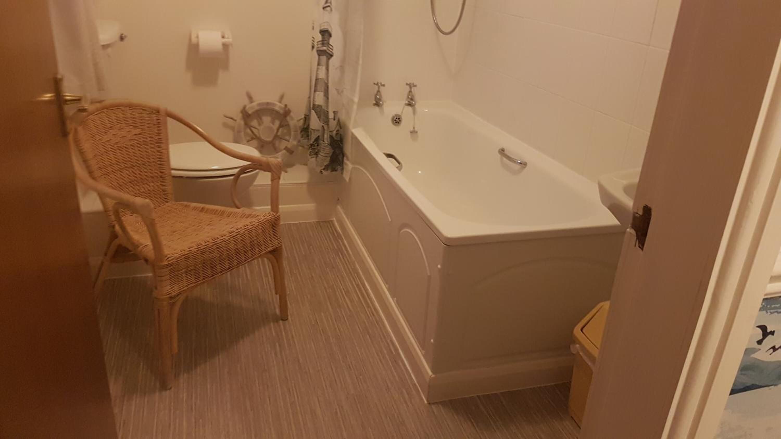 Une salle de bain avec un fauteuil en osier, des toilettes, une baignoire et une douche.