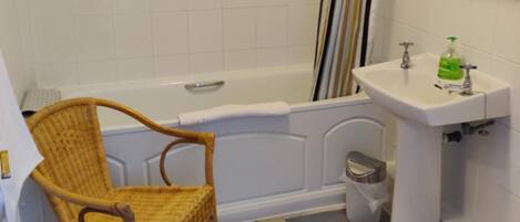 A bathroom with a bathtub, a wicker chair, a sink with a mirror, and patterned floor tiles.