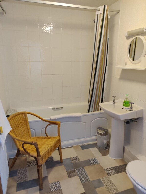 Un baño con bañera, una silla de mimbre, un lavabo con espejo y baldosas de suelo estampadas.