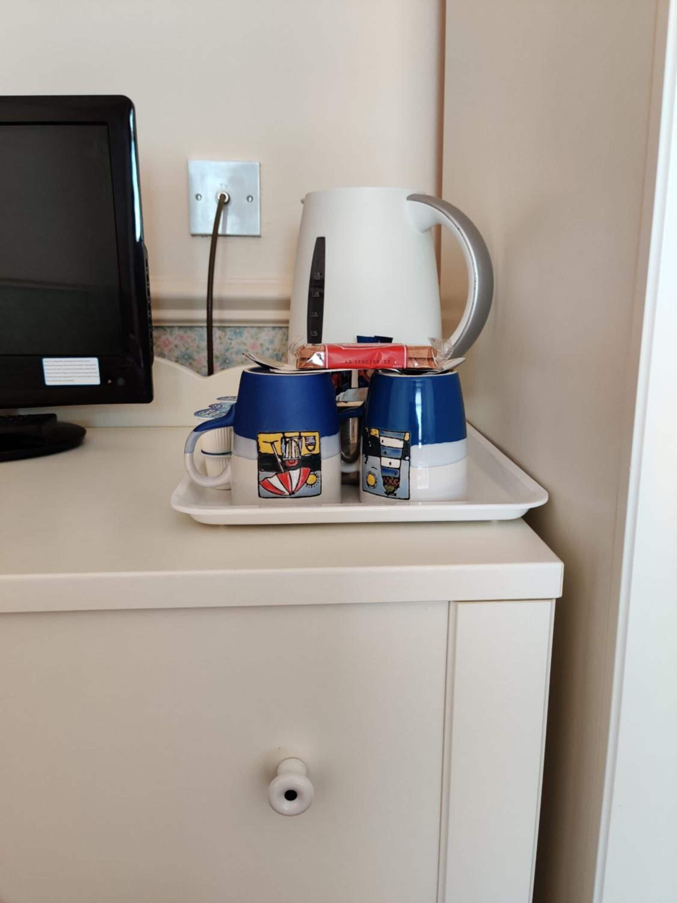 A kitchenette with a coffee maker, two mugs with cartoon designs, and a computer monitor.