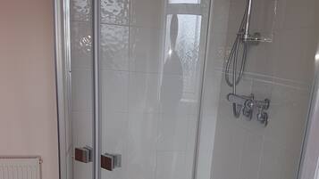A glass-enclosed shower area with a bathtub, a visible shower head, and a control panel.