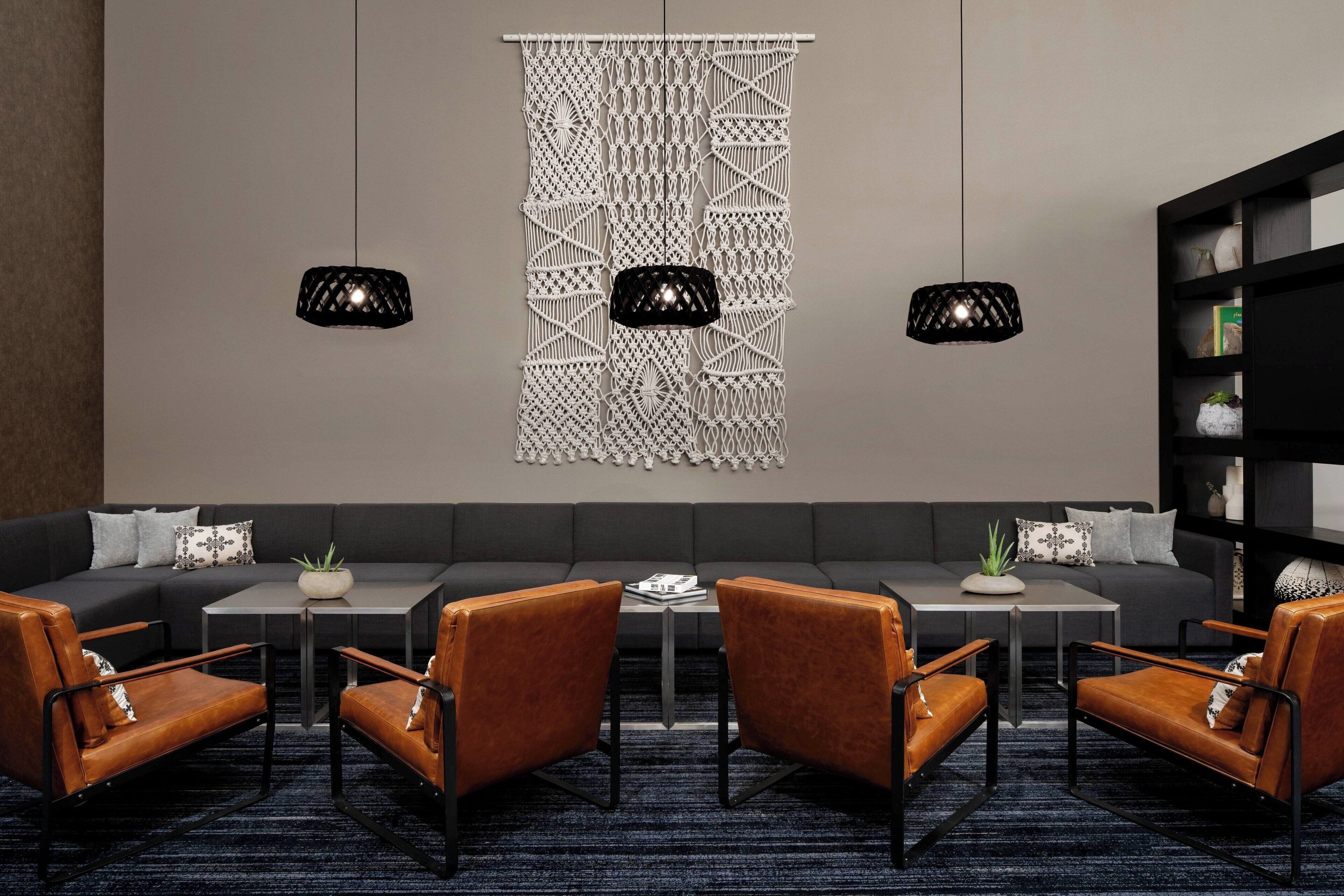 A modern lounge area with a sectional sofa, two black pendant lights, and a bookshelf.