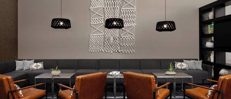 A modern lounge area with a sectional sofa, two black pendant lights, and a bookshelf.