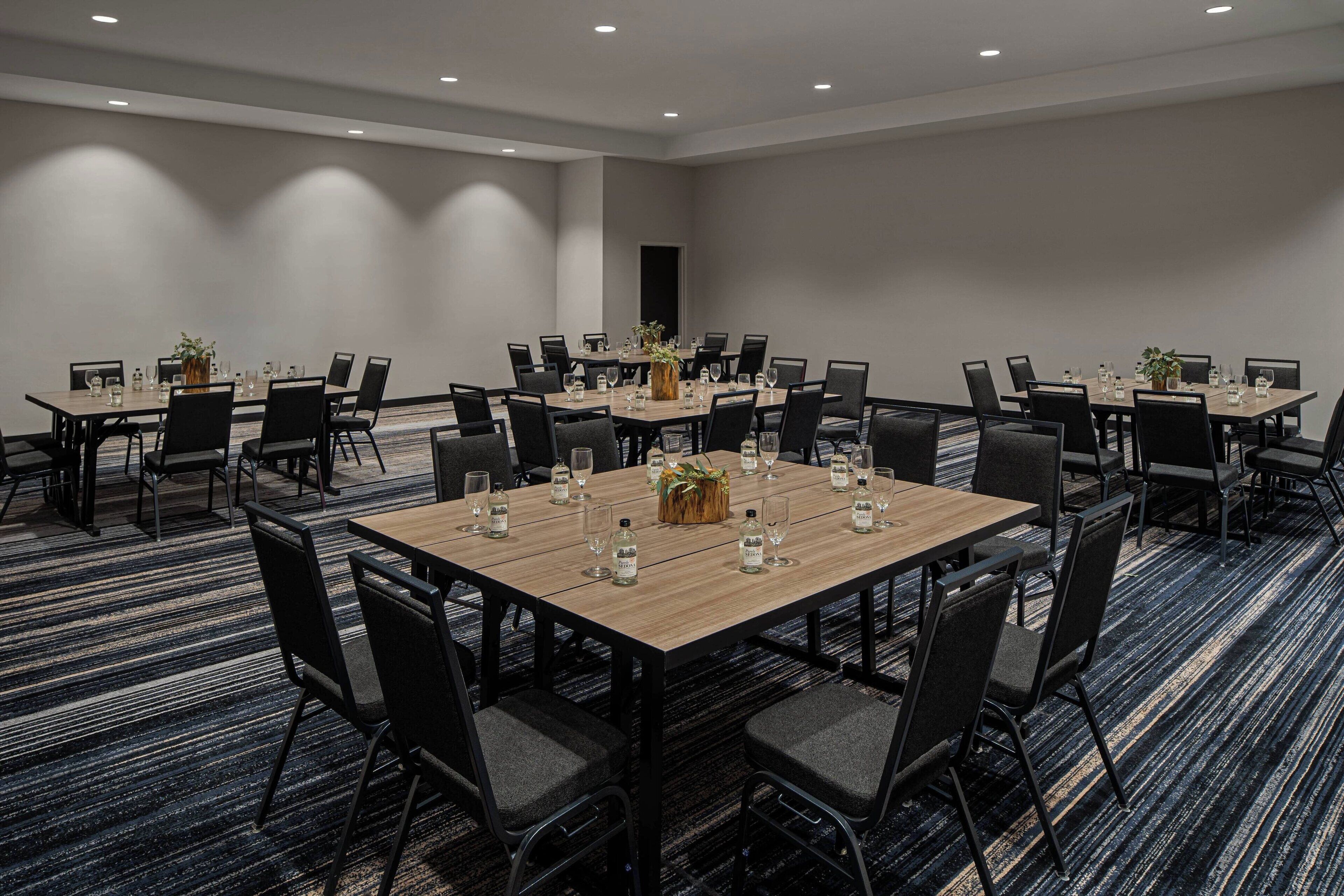 A conference room with multiple tables and chairs, equipped with water bottles and glasses, and a carpeted floor.