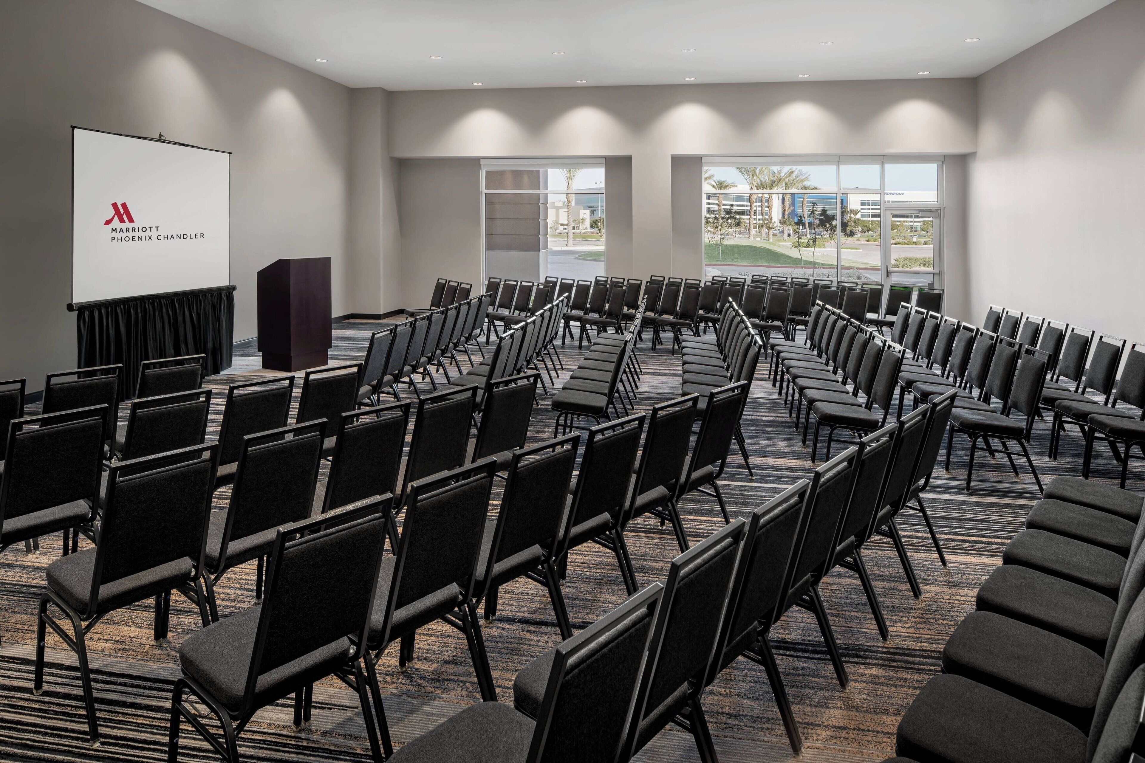 A conference room with rows of black chairs, a podium, and a projection screen with the Marriott Phoenix Chandler logo.