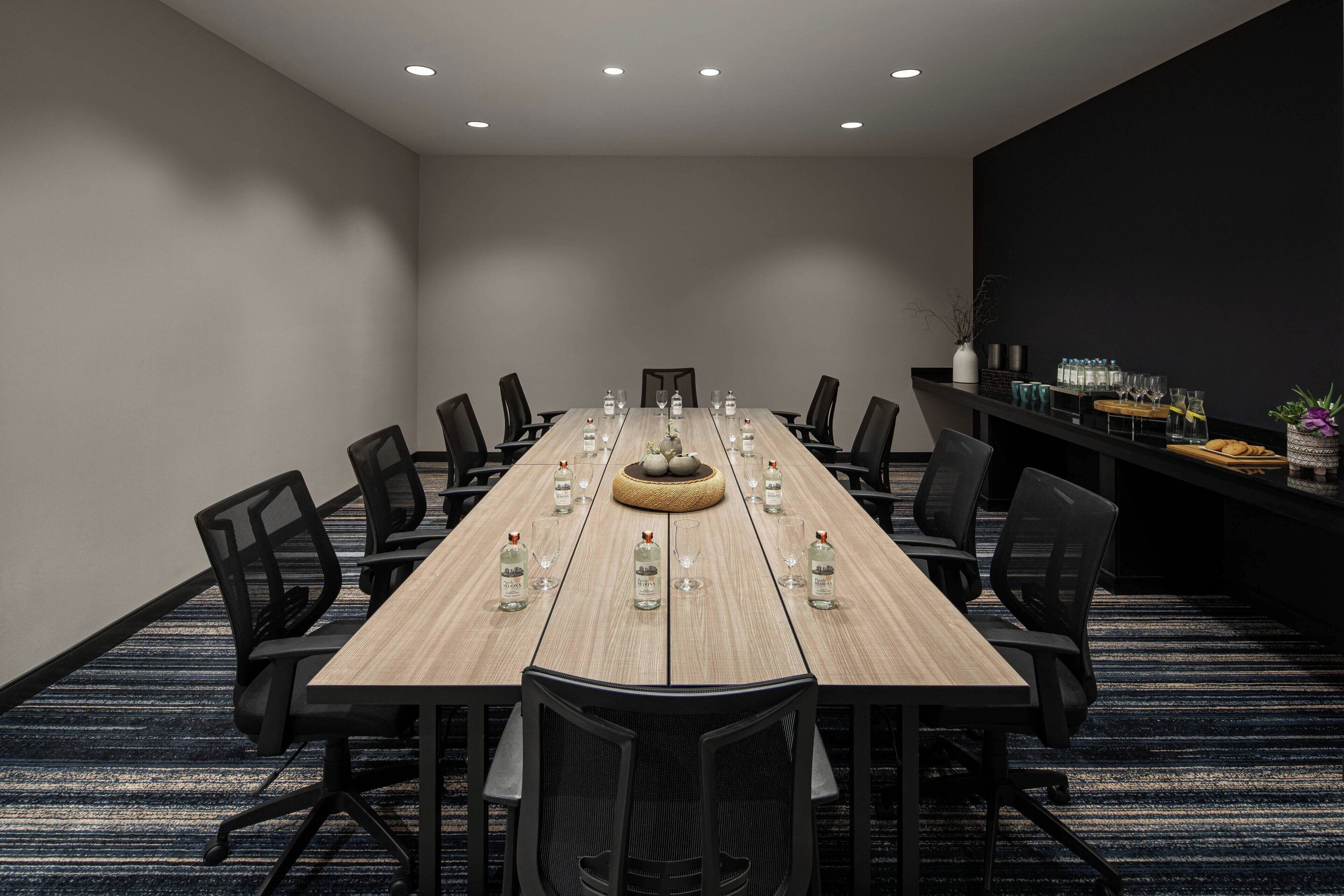 A conference room with a long table, chairs, and a bar area with glasses and bottles.