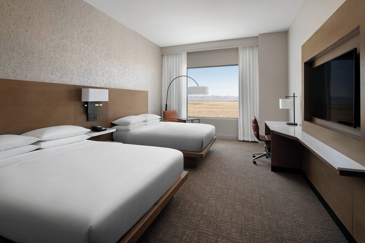 A hotel room with two beds, a desk, a TV, and a view of the desert.