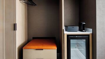 Una habitación pequeña con cama, un refrigerador compacto y una cafetera.