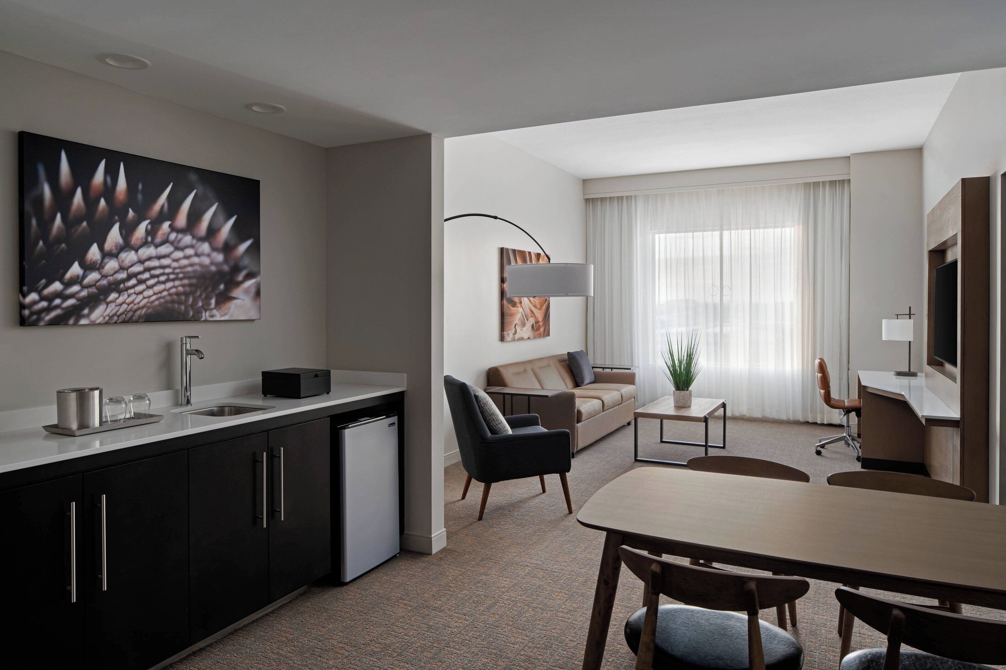 Een moderne hotelkamer met kitchenette, een zithoek, een bank en een groot raam met gordijnen.