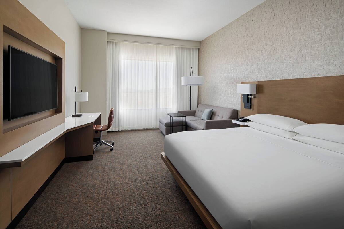 A hotel room with a large bed, a desk with a chair, a television, and a sofa.