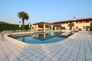 Una piscina con solárium de baldosas, una zona de estar cubierta y un edificio con tejado de baldosas.