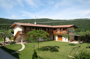 Una casa de dos pisos con balcón, jardín y vistas de las colinas circundantes.
