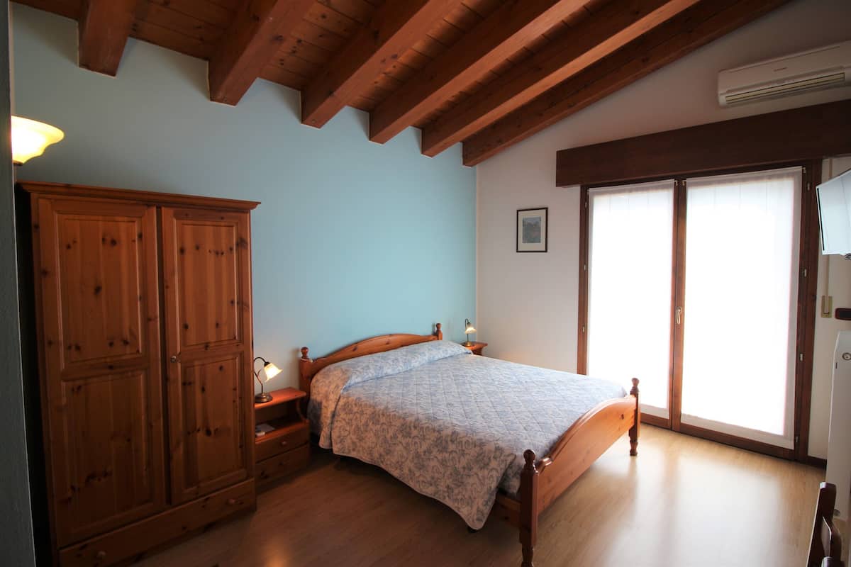 A bedroom with a wooden bed, a wardrobe, and a large window with blinds.