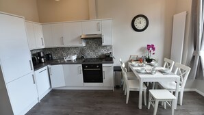 A modern kitchen with white cabinets, a black stove, and a dining area with white chairs and a table set for four.