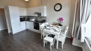 A modern kitchen with white cabinets, a black stove, and a dining area with white chairs and a table set for four.