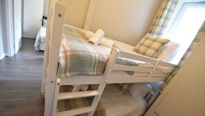 A bunk bed with a plaid bedspread and pillows, a small bedside table, and a window with curtains.