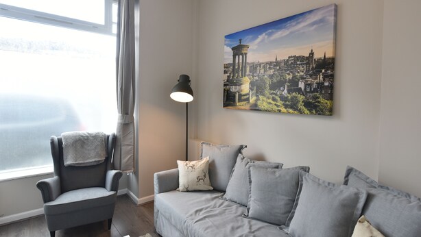 A modern living room with a grey sofa, a matching armchair, and a floor lamp. A cityscape painting adorns the wall.