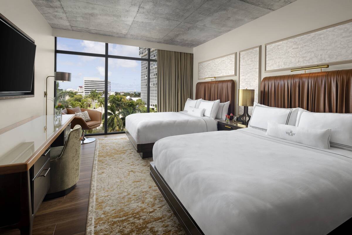 Een moderne hotelkamer met twee bedden, een bureau en een groot raam met uitzicht op de stad.