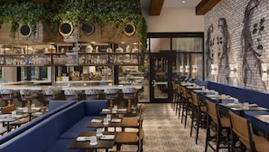 Un restaurante con zona de bar, asientos con cojines azules y un mural en la pared.