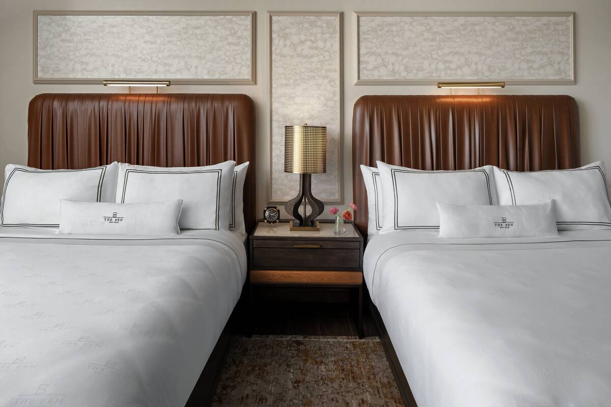 Een hotelkamer met twee bedden, een nachtkastje met een lamp en een lijst met kunstwerk erboven.