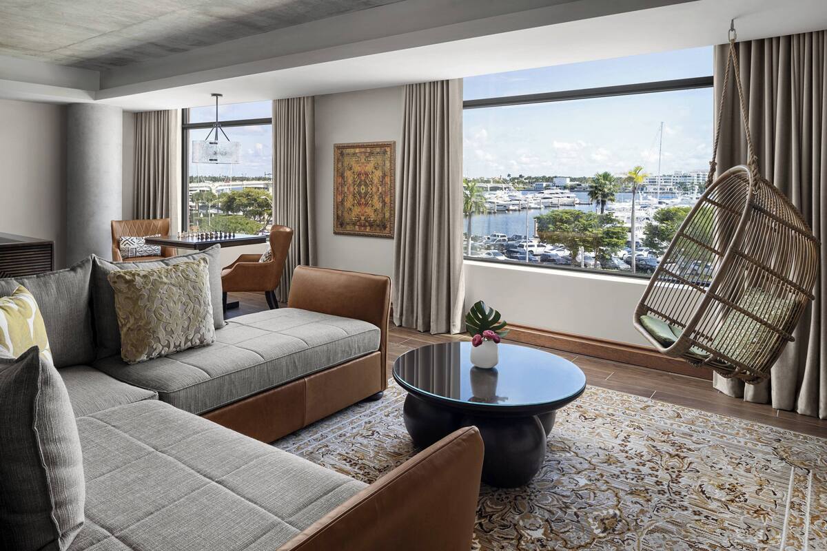 Een moderne woonkamer met een bank, fauteuils, een salontafel en uitzicht op een jachthaven.