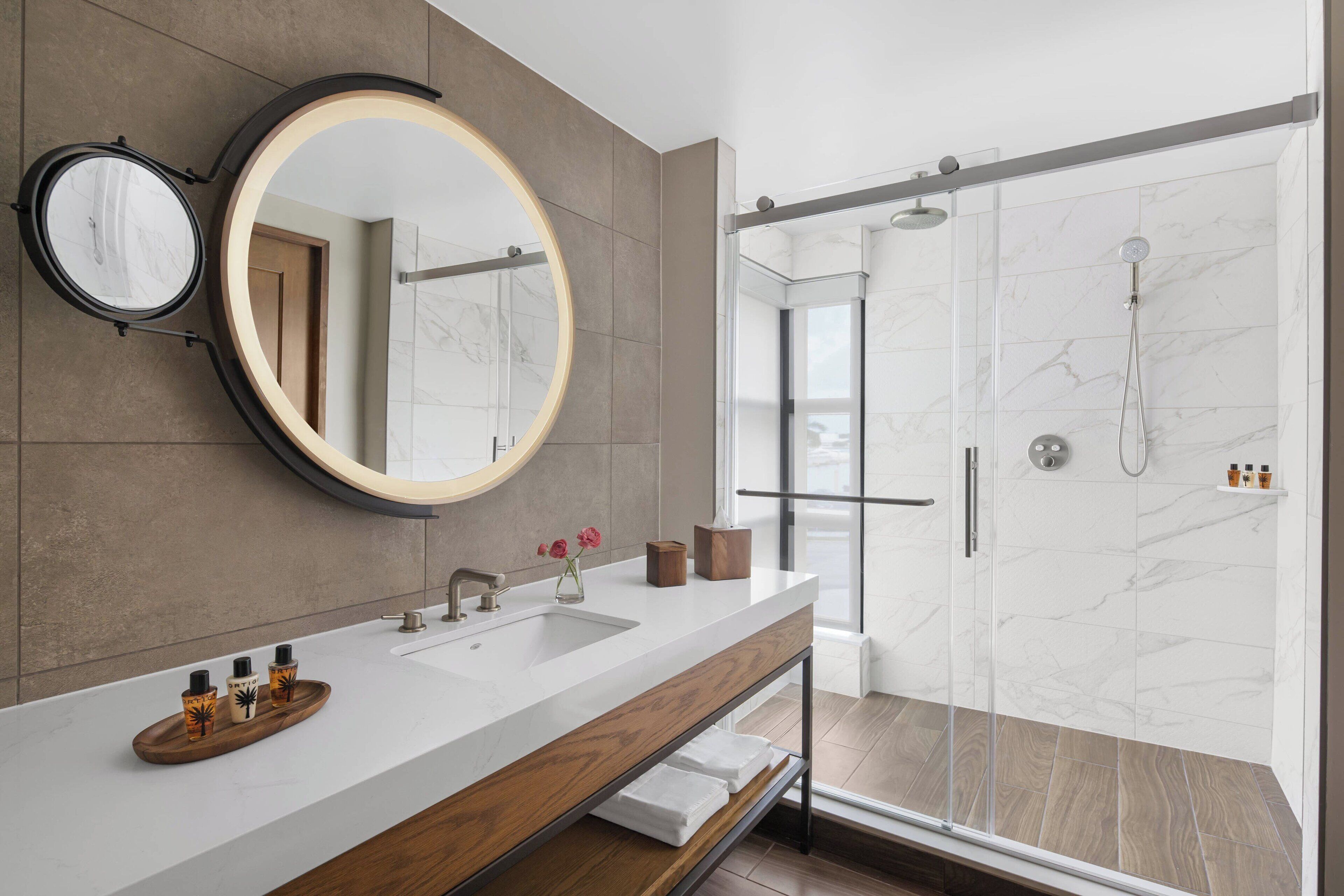 A modern bathroom with a large mirror, a shower, and a vanity with a tray of toiletries.