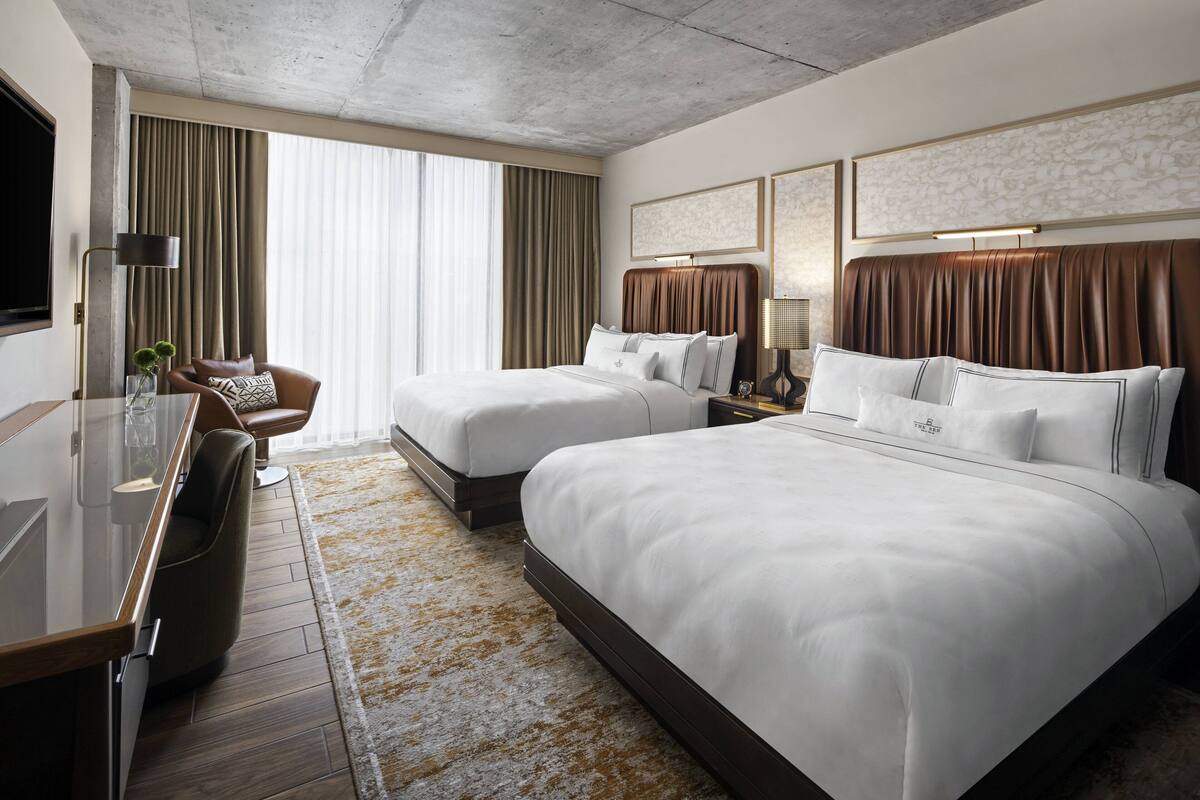 Een hotelkamer met twee bedden, een bureau, een stoel en een groot raam met gordijnen.