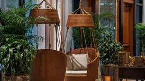 Sillones de mimbre con cojines, una mesa de madera y plantas en macetas en un área de recepción.