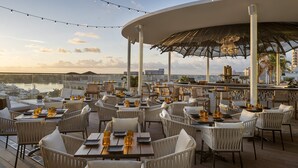 Un área de comedor al aire libre con mesas, sillas y un bar, con vista al agua.