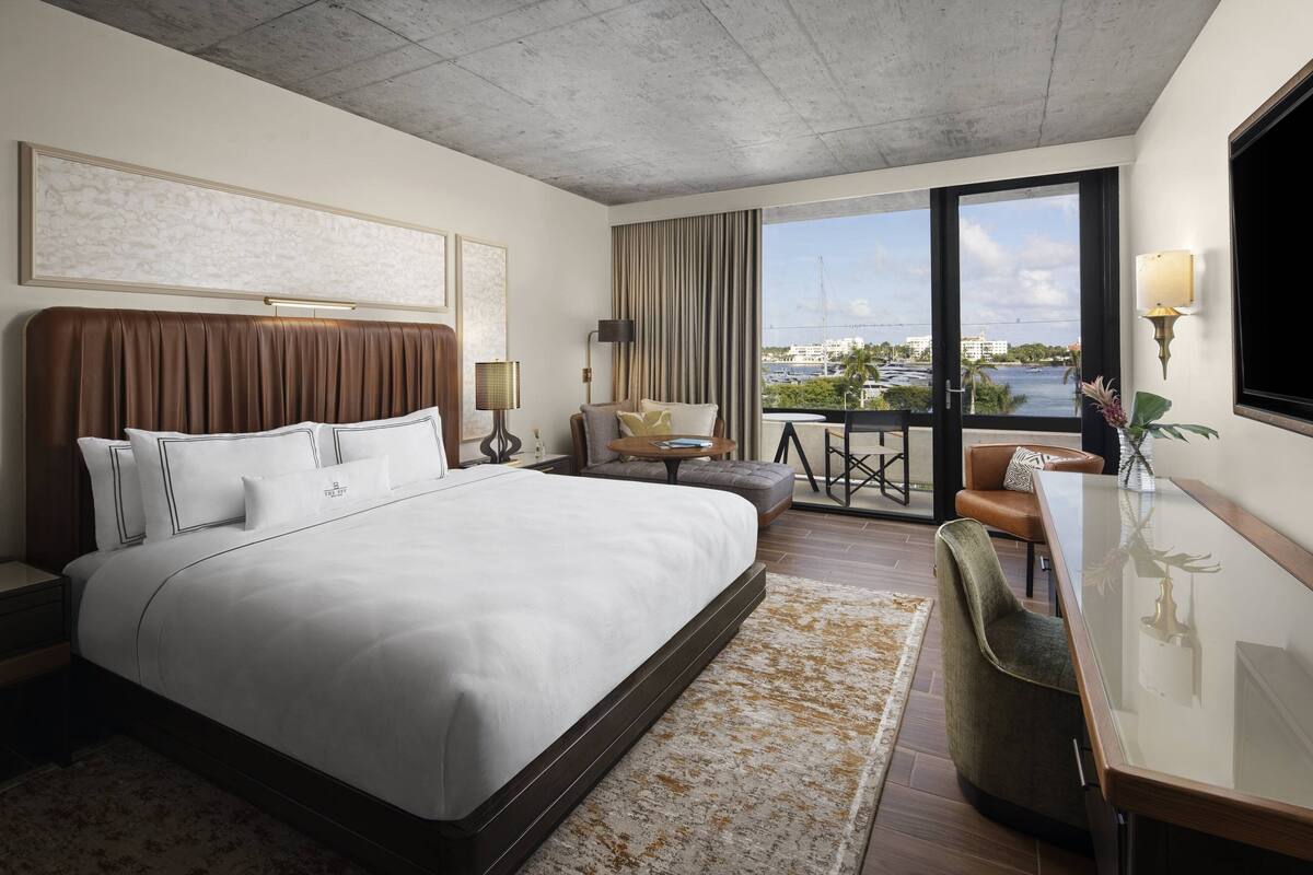 Een hotelkamer met een groot bed, een bureau, een stoel, uitzicht op het water en een balkon.