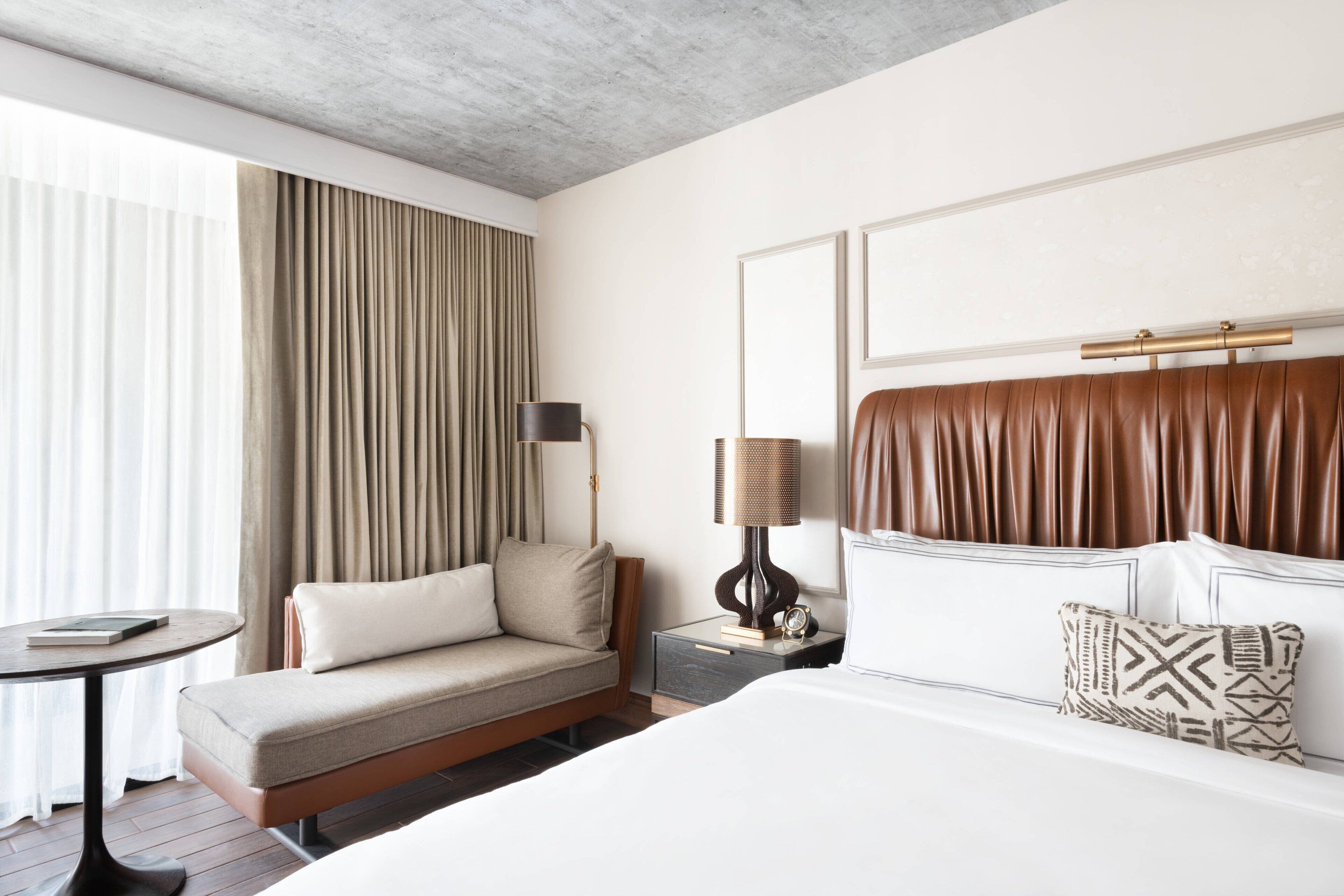 Habitación de hotel con cama, sofá, mesita de noche, lámpara y vistas al exterior.