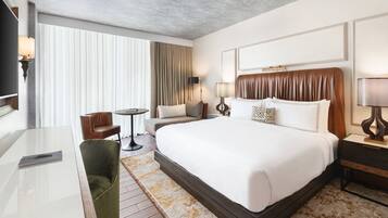 Quarto de hotel moderno com uma cama grande, uma escrivaninha, uma cadeira e uma mesa pequena.
