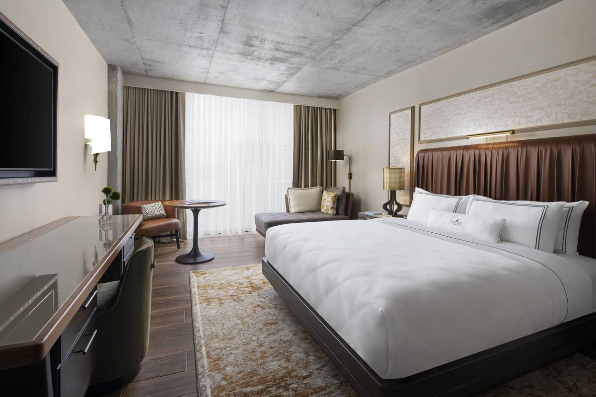 Een moderne hotelkamer met een groot bed, een bureau, een stoel, een televisie en een raam met gordijnen.