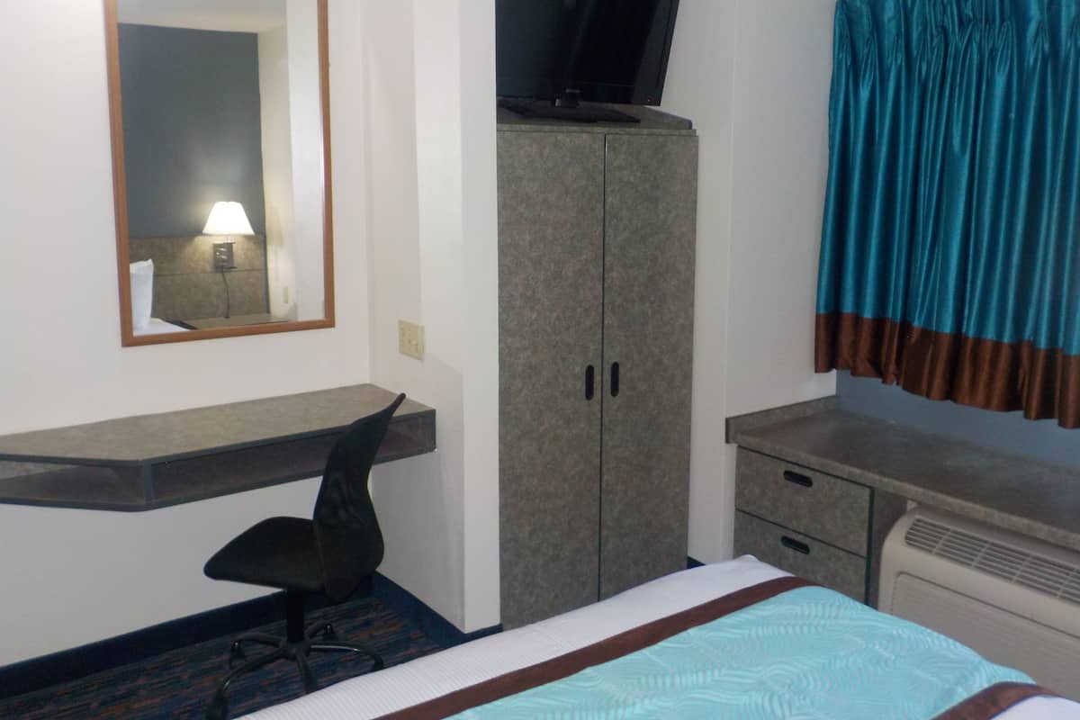 A hotel room with a bed, a desk with a chair, a television on top of a cabinet, a mirror on the wall, and a window with curtains.