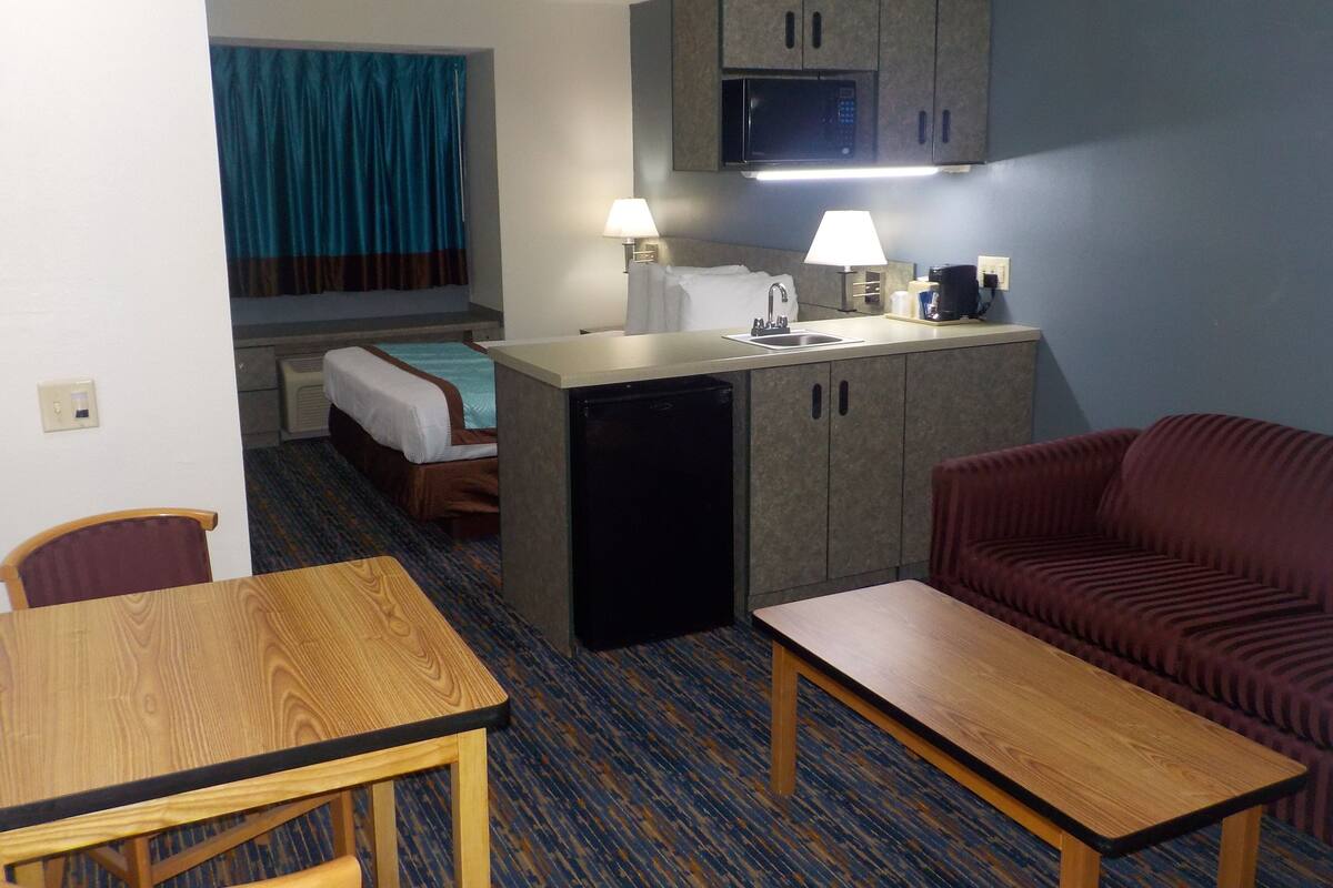 A compact hotel room with a kitchenette, a bed, a sofa, a dining table, and a small refrigerator.