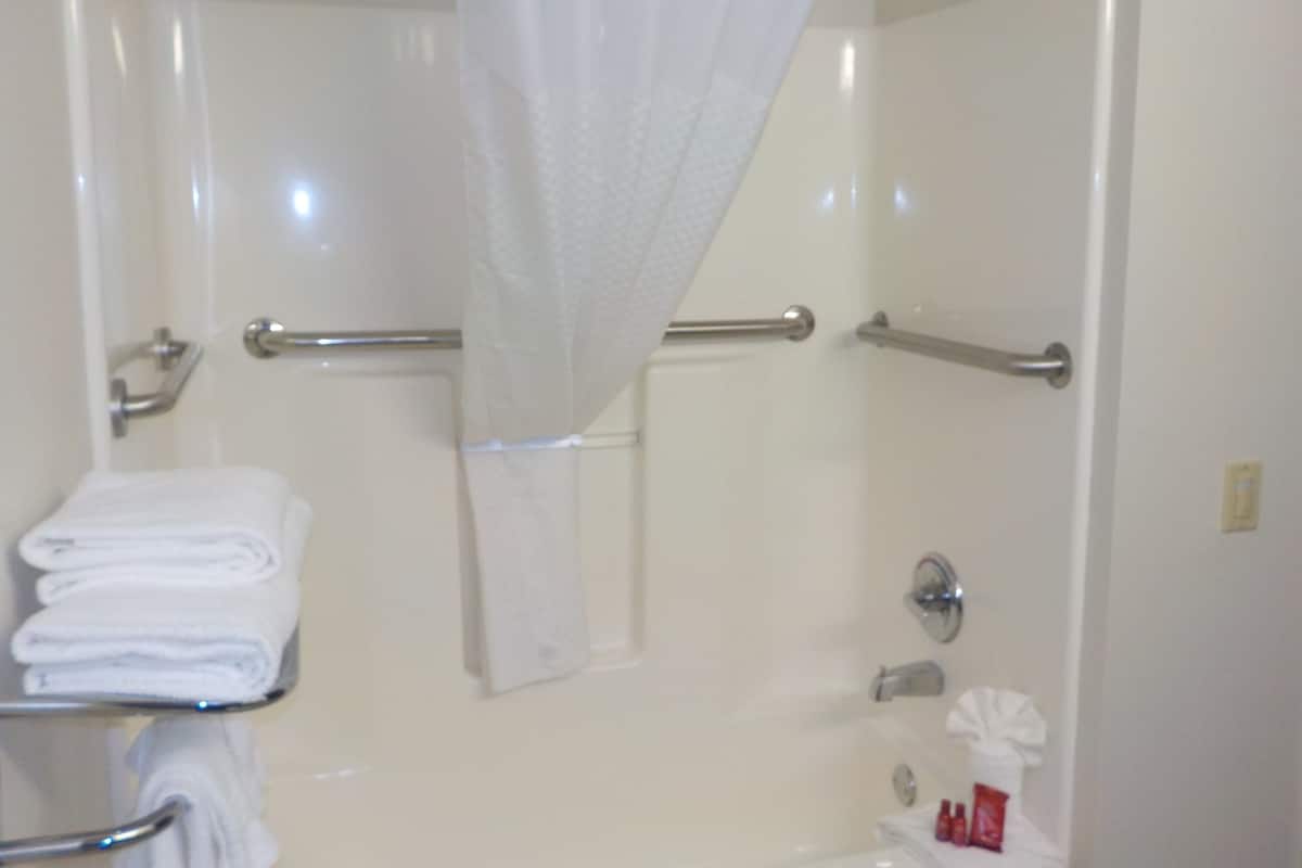 A bathroom with a shower, a towel rack, and a handrail.