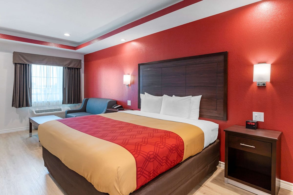 A hotel room with a large bed, a desk, a chair, and a nightstand with a clock.