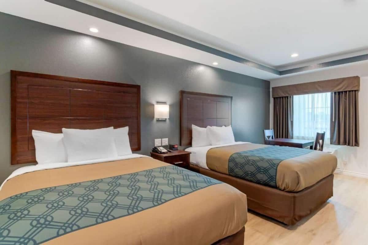 A hotel room with two beds, a desk, a chair, and a window with curtains.